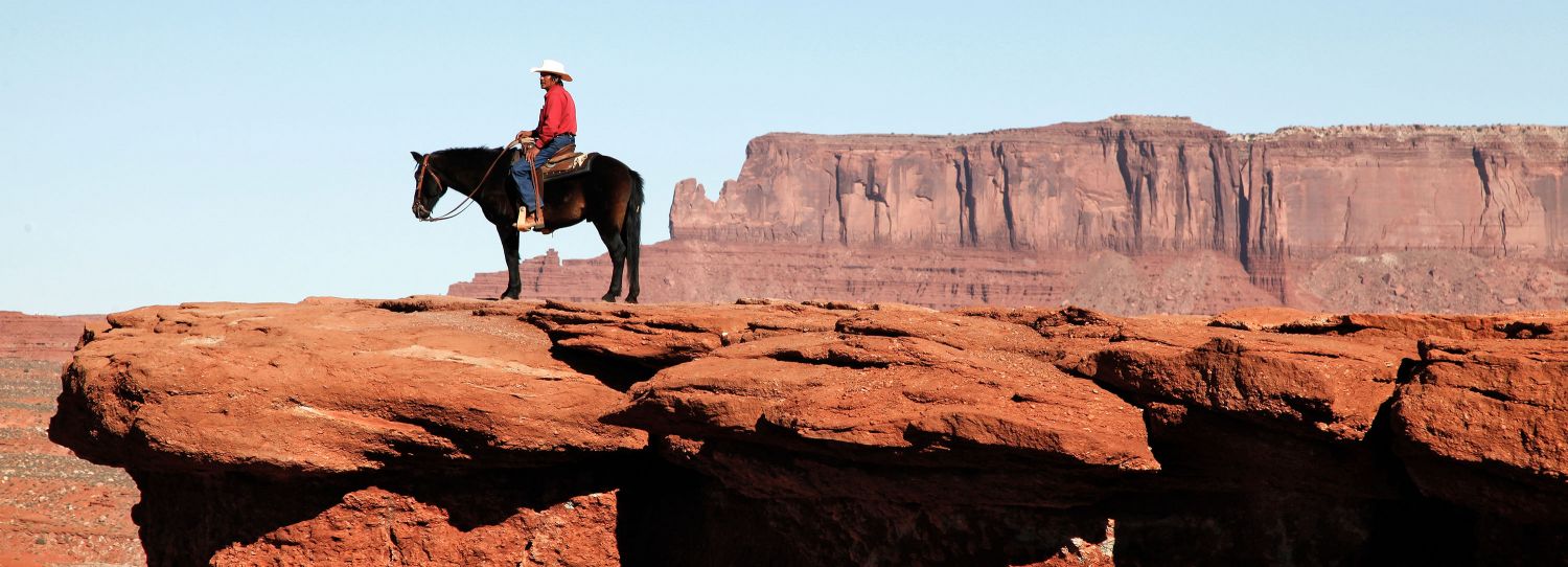 A panoramic image of John Ford Point, Monument Valley with a Navajo Indian on Horseback